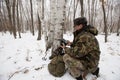 An employee of the national park in green camouflage clothes sets a camera trap on a tiger or leopard in a birch forest