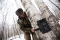 An employee of the national park in green camouflage clothes sets a camera trap on a tiger or leopard in a birch forest