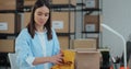 An employee packs a yellow jumper in a room with shelves full of parcels. The woman owner of an online store works on a