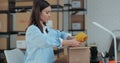 An employee packs a yellow jumper in a room with shelves full of parcels. The woman owner of an online store works on a