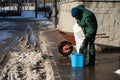 An employee pours expanded clay from the bag into a bucket, which he will use to sprinkle pavements