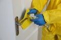 Employee in protective suit and gloves sanitizing door knob indoors, closeup. Medical disinfection