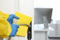 Employee in protective suit and gloves sanitizing door knob indoors, closeup. Medical disinfection