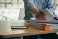 An employee sits at a table full of paper. stamp on the pile of unfinished documents A young account manager`s secretary works in