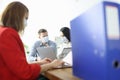 Employees in office are sitting at table wearing protective medical masks