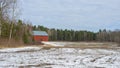 Empty agriculture fields in winter covered with first snow. Winter crops. Red wooden farm house or barn background. Silhouettes of Royalty Free Stock Photo