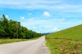 empty asphalt country road along the wall of dam with green grass and blue sky with clouds and mountain background in countryside. Royalty Free Stock Photo