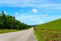 empty asphalt country road along the wall of dam with green grass and blue sky with clouds and mountain background in countryside Royalty Free Stock Photo