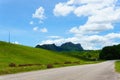 empty asphalt country road along the wall of dam with green grass and blue sky with clouds and mountain background in countryside Royalty Free Stock Photo