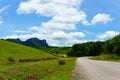 Empty asphalt country road along the wall of dam with green grass and blue sky with clouds and mountain Royalty Free Stock Photo