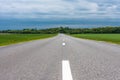 Empty asphalt country road with green grass fields under stormy clouds in the summer Royalty Free Stock Photo