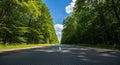 Empty asphalt road stretching through a dense green forest under a blue sky with white clouds Royalty Free Stock Photo