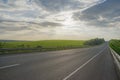 Empty asphalt road at sunset. Cloudy sky and green meadows Royalty Free Stock Photo