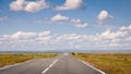 Empty asphalt road to the horizon through autumn steppe under blue sky with clouds. Royalty Free Stock Photo