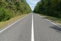 Empty asphalt road through woods and fields. New fresh asphalt pavement away from the city. Development of rural infrastructure. Royalty Free Stock Photo