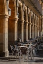 Empty bar tables and wicker chairs from a medieval restaurant next to the columns and arches of the main square in Salamanca