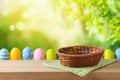 Empty basket with tablecloth and Easter eggs on wooden table over green bokeh background. Easter mock up for design and product