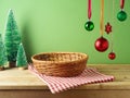 Empty basket on wooden table with hanging ornamenrt decoration and tablecloth over green background. Christmas mock up for design Royalty Free Stock Photo