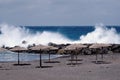 An empty bay made of lava sand beach in Corona times without people and without sun loungers, but with a row of open straw