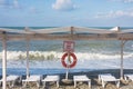 Empty beach with sun loungers. Sea or ocean in storm with big waves. Life buoy and sign with inscription in Russian