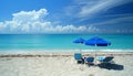 Empty beach with two blue sunshades and three deck chairs in front of the blue ocean Royalty Free Stock Photo