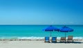 Empty beach with two blue sunshades and three deck chairs in front of the blue ocean Royalty Free Stock Photo