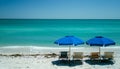 Empty beach with two blue sunshades and three deck chairs in front of the blue ocean Royalty Free Stock Photo