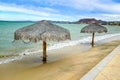 Empty beach with two palapas next to promenade, sea and mountains in background Royalty Free Stock Photo