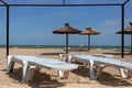 Empty beach view with white plastic chaise lounges deck chairs, awning and straw umbrellas parasol