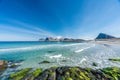 Empty beautiful beach during springtime on sunny day with blue sky and silent ocean with small waves and mountain chain with snow Royalty Free Stock Photo