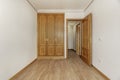 Empty bedroom with a built-in three-door oak wardrobe with handles, a skirting board of the same material, smooth white painted