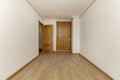 Empty bedroom with a built-in wardrobe with two oak wood doors with handles, a skirting board of the same material, smooth white