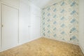 Empty bedroom with white wooden venetian style door cabinet on one wall, walls with blue patterned wallpaper and light oak parquet