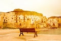 Empty bench on pier in Cefalu, Sicily, Italy in orange sunlight with historical buildings on the sea coast. Sunrise, sunset. Peace Royalty Free Stock Photo