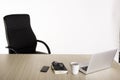 An empty black armchair at a wooden desk with a open laptop, cup of coffee, notebook, reading glasses and mobile phone. Royalty Free Stock Photo