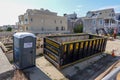 An empty black dumpster and a portable toilet are seen at a construction site near a backhoe