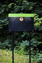 Empty black and green metal sign board with a question mark on it in the forest