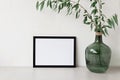 Empty black picture frame mockup, copy space, green glass vase with willow tree branches on beige tabletop and beige Royalty Free Stock Photo