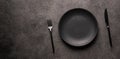 an empty black plate and a fork with a knife on a dark background. Flatlay photo, mockup concept for advertising and Royalty Free Stock Photo