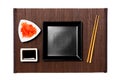 Empty black square plate with chopsticks for sushi, ginger and soy sauce on dark bamboo mat background. Top view with copy space Royalty Free Stock Photo