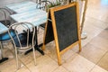 Empty blackboard space for menu on tiled floor, tables and chairs near. Mockup to add your own text