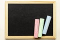 Empty blackboard with three colored crayons. Pink, blue and green chalk on a black chalkboard. With place for text. Royalty Free Stock Photo