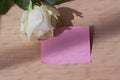 Empty blank pink paper note and white rose on wood table with window light Royalty Free Stock Photo