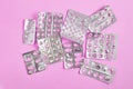 empty blister packs of pills with one partially full pack on pink background.