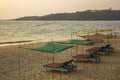 Empty blue beach beds under color awnings on the yellow sand against the background of the sea and the green island with the house Royalty Free Stock Photo