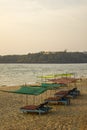 Empty blue beach beds under color awnings on the yellow sand against the background of the sea and the green island with the house Royalty Free Stock Photo