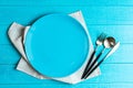 Empty blue ceramic round plate with table cloth,knife,spoon and fork on blue wooden background Royalty Free Stock Photo