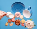 Empty blue cup, donuts, macaroons, peony and hand holding  milk cream jug flying over  blue background Royalty Free Stock Photo