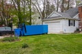 An empty blue dumpster in the driveway of a house.