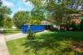 An empty blue dumpster in the driveway of a house with its garage door open in a residential community Royalty Free Stock Photo